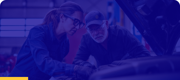 Two automotive technicians inspecting a vehicle engine together in a repair shop.