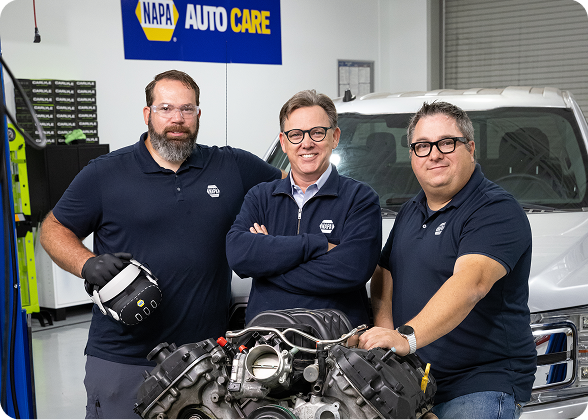 Team members in an automotive training workshop with an engine and filming equipment
